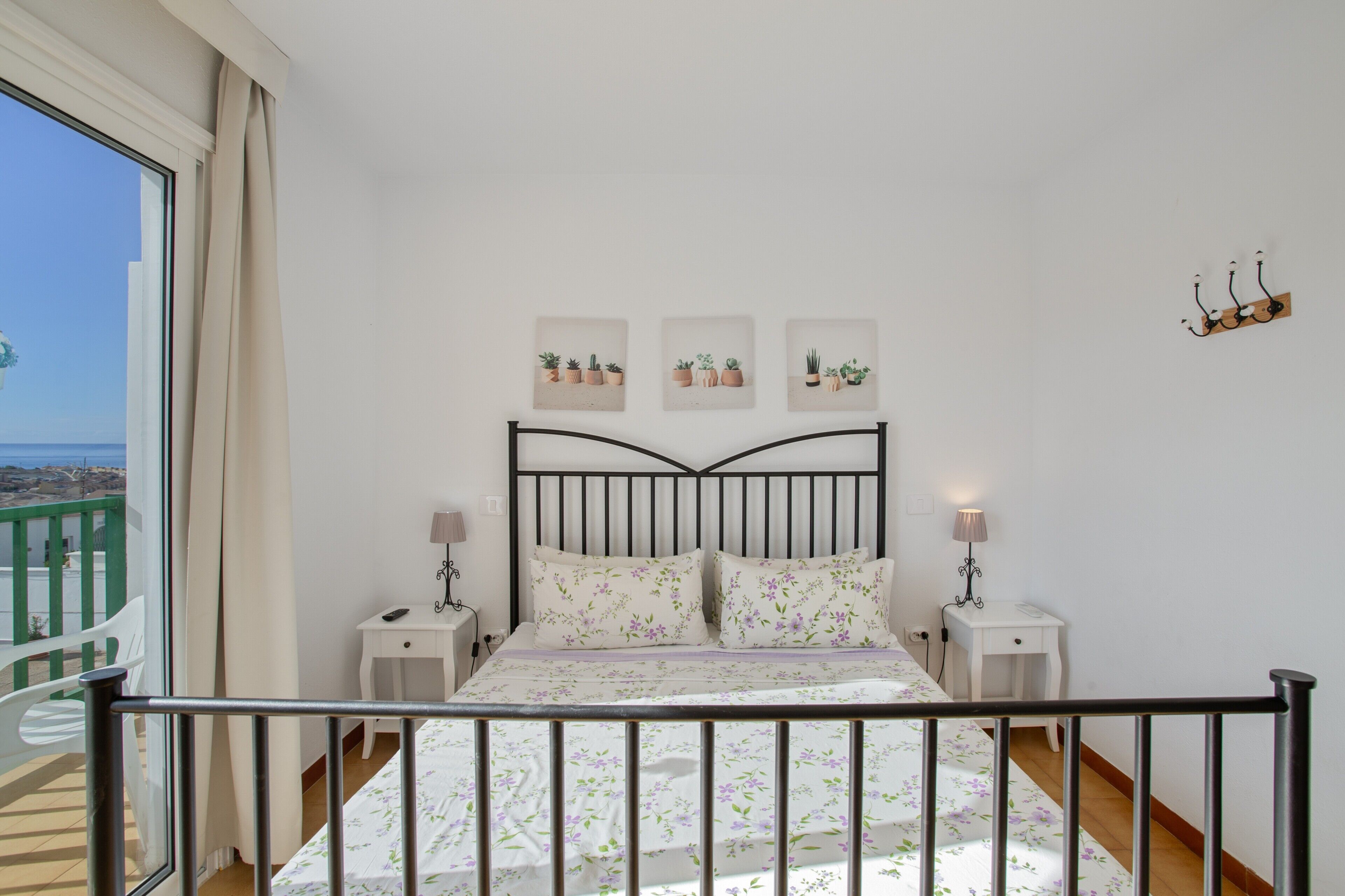 A bedroom with a bed, bedside tables, a view of the balcony, and wall-mounted artwork.