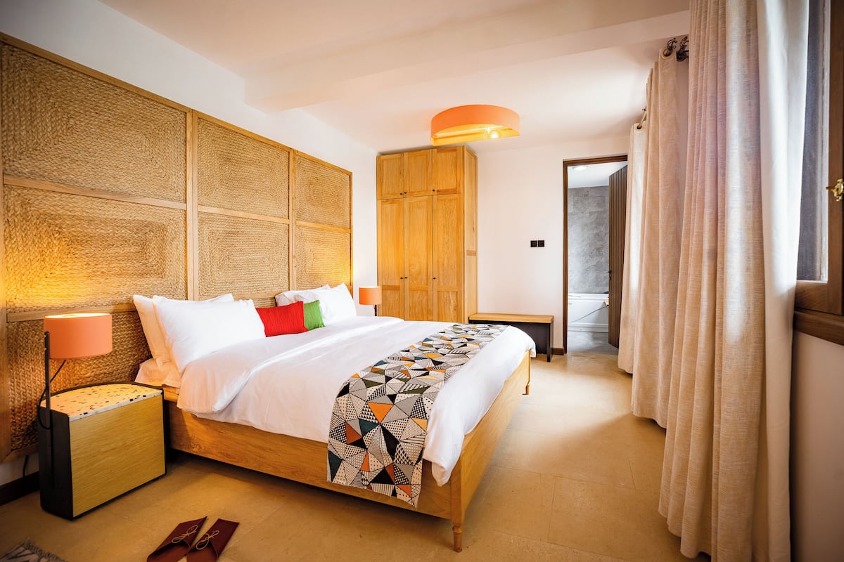 A hotel room with a wooden bed, a bedside lamp, a geometric patterned throw, and a wooden wardrobe.