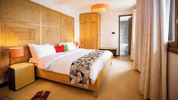A hotel room with a wooden bed, a bedside lamp, a geometric patterned throw, and a wooden wardrobe.