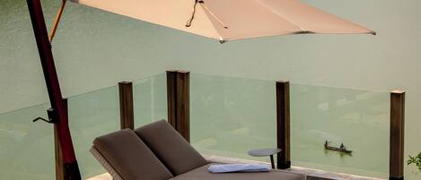 A poolside lounge with a cushioned seating area, a glass balustrade, and a view of a lake.