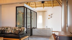 A modern bathroom with a bathtub, a glass-enclosed shower, and a sofa with tropical prints. - Tabebuia Spa & Safari Resort (Fort Portal)