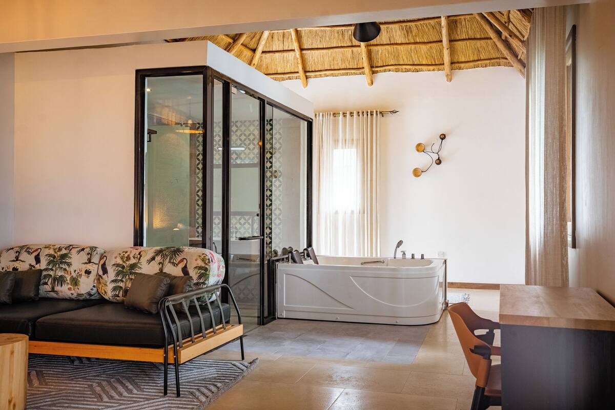 A modern bathroom with a bathtub, a glass-enclosed shower, and a sofa with tropical prints.