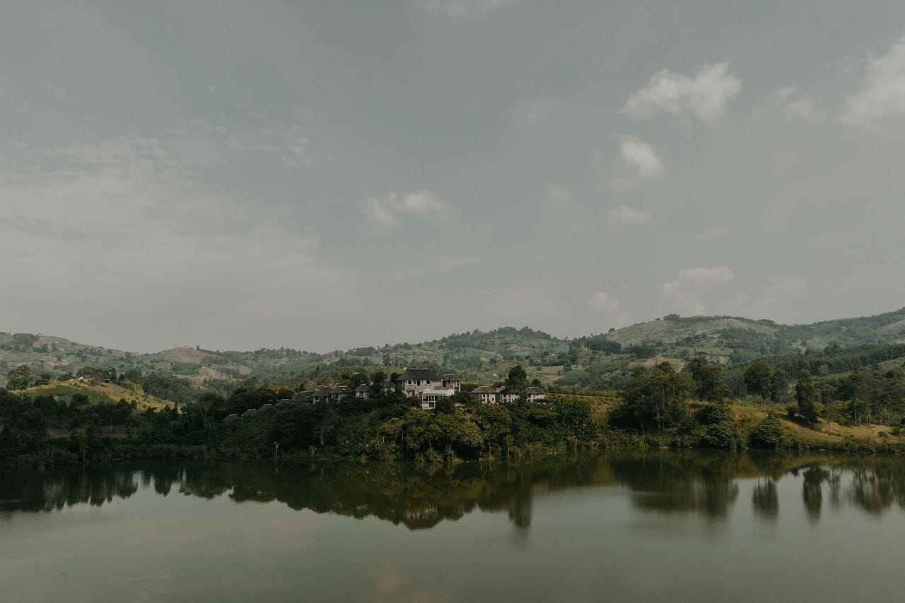 A lakeside property with a house surrounded by lush greenery and hills in the background.
