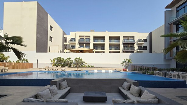 A modern outdoor pool area with lounge chairs and a seating area, surrounded by a building with balconies. - Manzil- Chic 2BR w Pool nr Circle Mall  (Dubai)