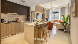 A modern kitchen with a marble countertop, wooden cabinets, and a central island with bar stools. - Manzil- Chic 2BR w Pool nr Circle Mall  (Dubai)