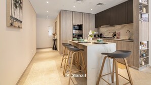 A modern kitchen with wooden cabinets, a marble countertop, and a central island with bar stools. - Manzil- Chic 2BR w Pool nr Circle Mall  (Dubai)