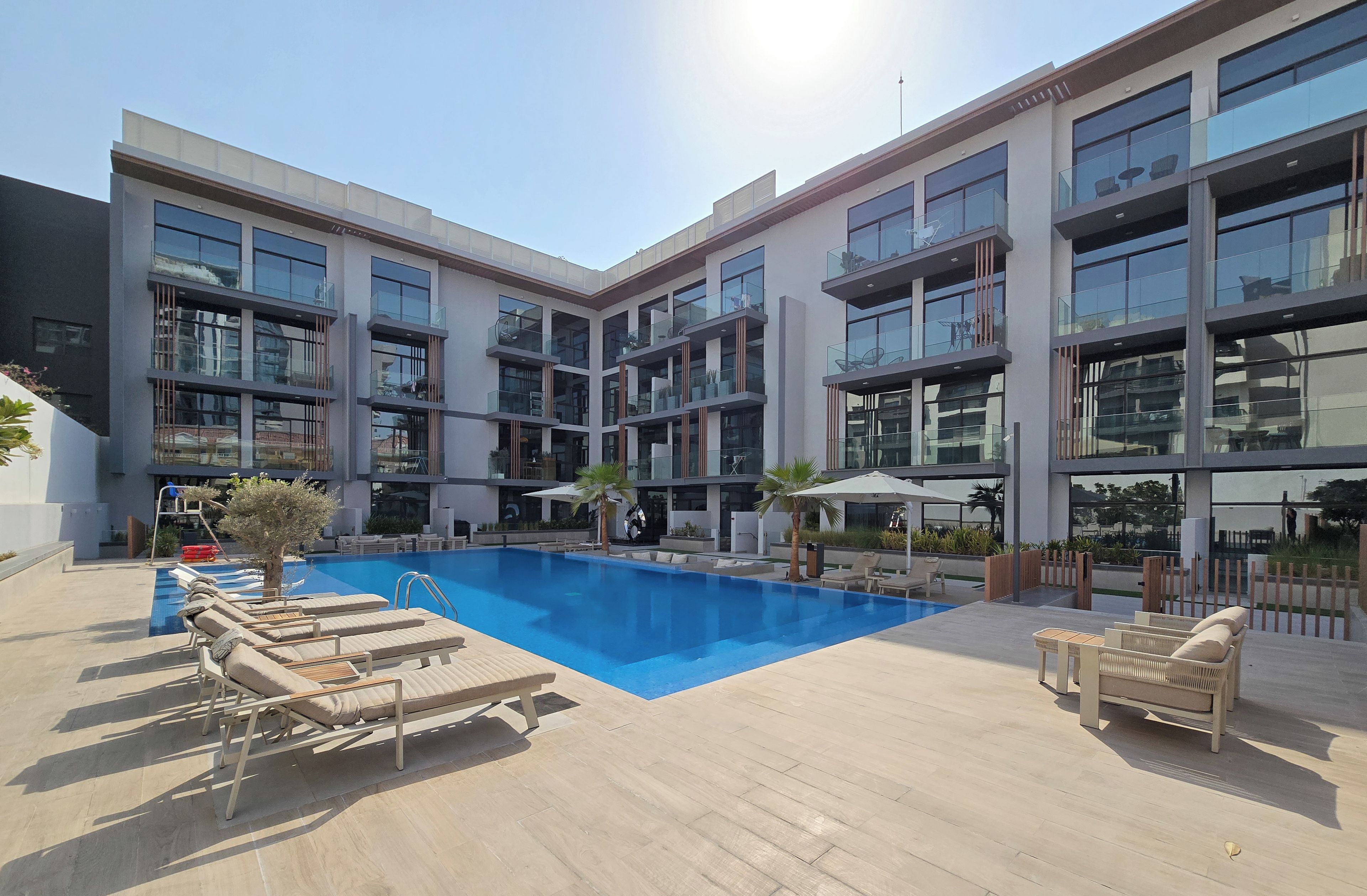 A modern building with a swimming pool, lounge chairs, and outdoor seating.
