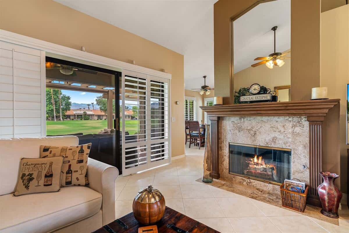 A living room with a fireplace, a sofa with decorative pillows, a coffee table with a pumpkin, and a view of a golf course through the sliding glass doors.