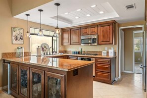 A kitchen with wooden cabinets, a stainless steel microwave, and a large island with a glass-fronted cabinet.