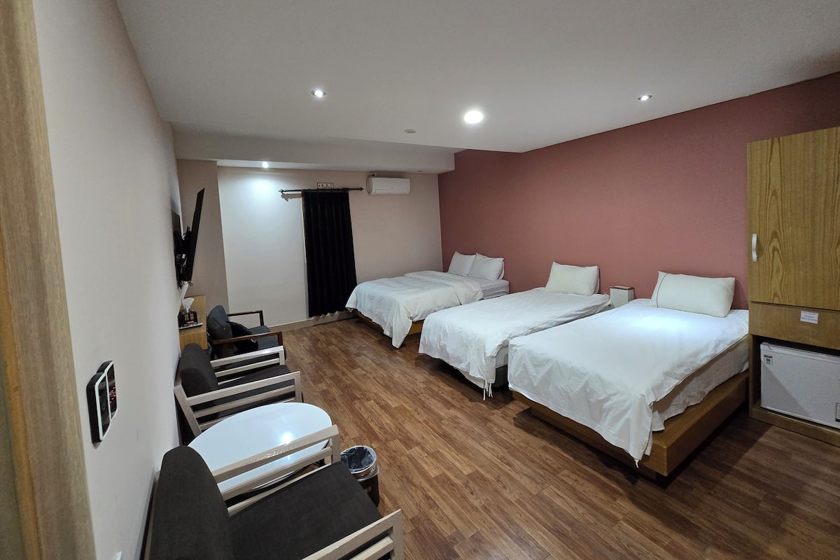 Una habitación de hotel con dos camas, un escritorio, una silla, suelo de madera y un armario.