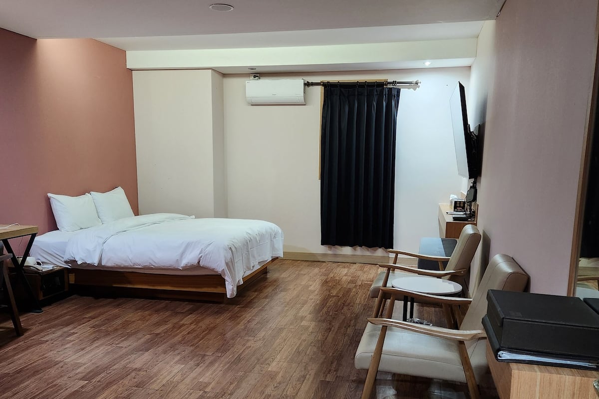 Una habitación de hotel moderna con suelo de madera, una cama, un escritorio, una silla y un televisor.