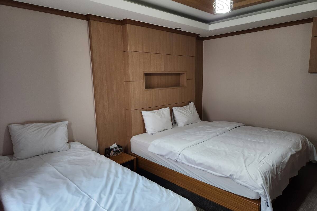 Habitación de hotel con dos camas, cabeceros de madera y una mesita de noche con un libro.