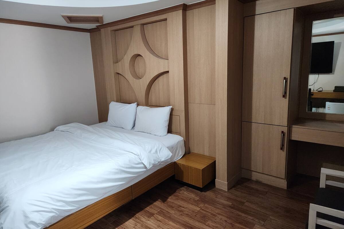 Un dormitorio moderno con cabecera de madera, cama con ropa de cama blanca, una mesita de noche y armarios empotrados de madera.