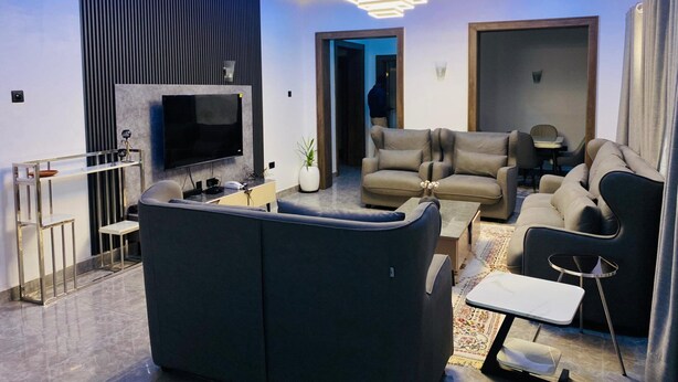 A modern living room with a flat-screen TV, a sofa, a coffee table, and a dining area. - Blooming Apartments (Jimeta)