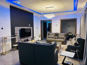 A modern living room with a flat-screen TV, a sofa, a coffee table, and a dining area. - Blooming Apartments (Jimeta)
