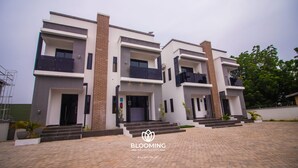 A modern multi-story apartment building with a brick facade, large windows, and a landscaped entrance area. - Blooming Apartments (Jimeta)