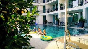 An indoor swimming pool with multiple levels of balconies, lounge chairs, and potted plants. - Blooming Apartments (Jimeta)