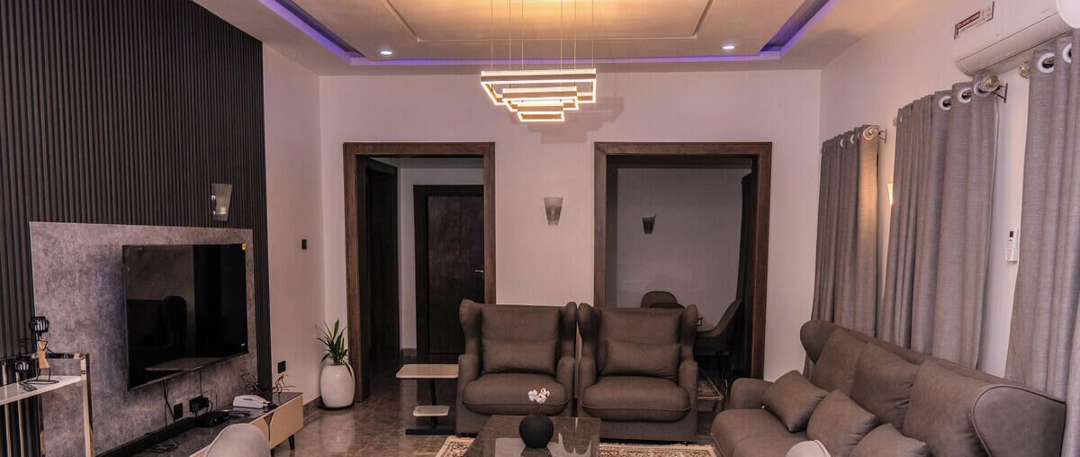 A modern living room with a grey sofa, two armchairs, a coffee table, and a flat-screen TV mounted on the wall.