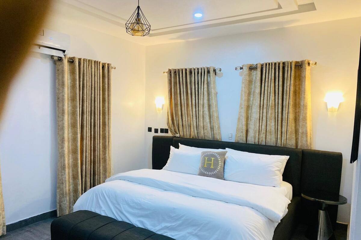 Une chambre d’hôtel avec un lit, une table de chevet, une lampe fixée au mur et des rideaux.