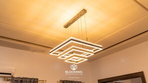 A modern chandelier with geometric design in a room with a white wall and a logo for 'BLOOMING APARTMENTS'. - Blooming Apartments (Jimeta)
