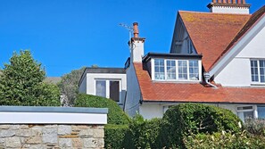 Una casa de dos pisos con techo de tejas rojas, una chimenea y una ventana con marcos blancos.