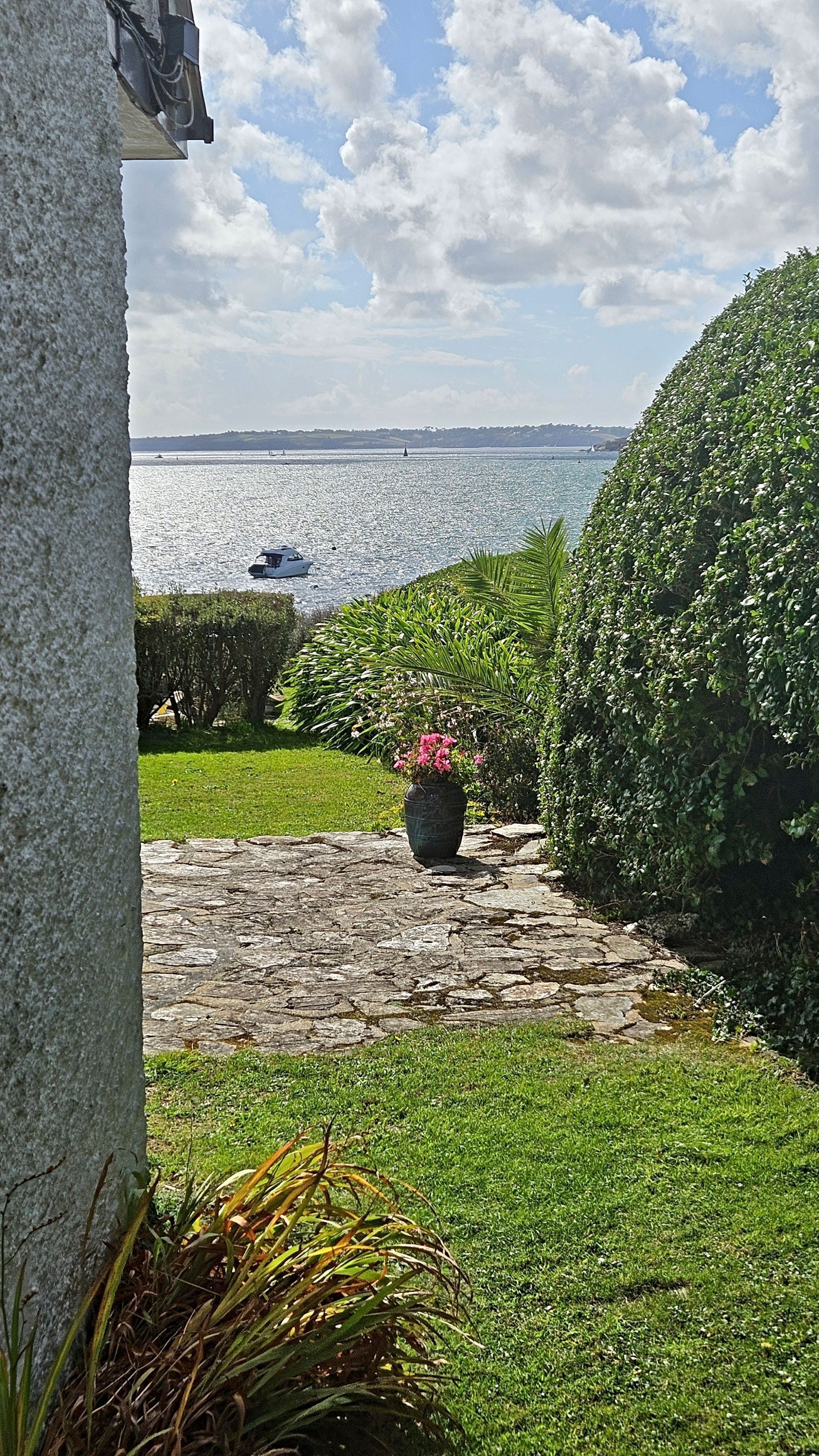 Un sendero de piedra que conduce a una zona verde con vista al mar y un velero a lo lejos.