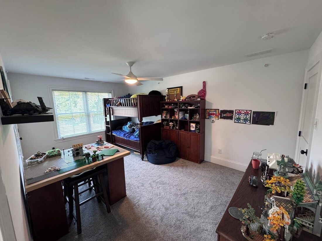 Een kamer met een stapelbed, een bureau met stoel, een boekenkast en een raam met jaloezieën.
