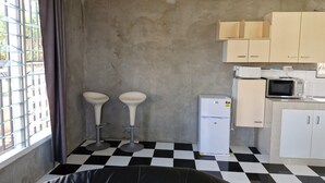 Kompakti keittiö, jossa on jääkaappi, mikroaaltouuni ja kaksi jakkaraa.
