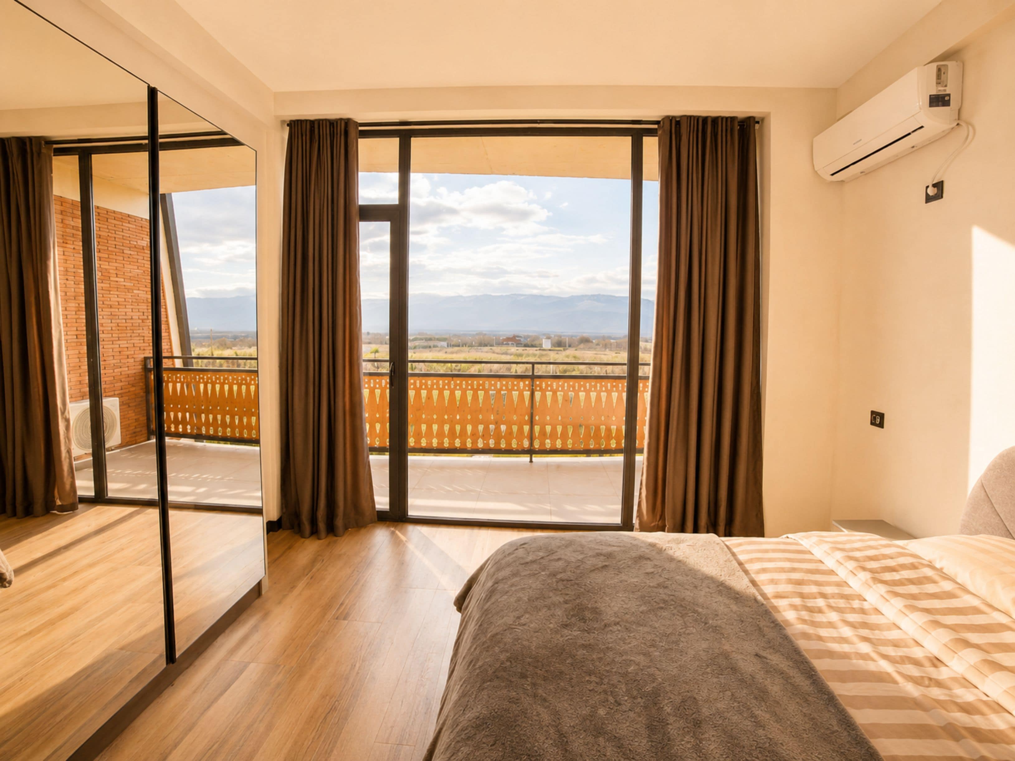 Habitación de hotel con un ventanal grande, una cama, piso de madera y un equipo de aire acondicionado.