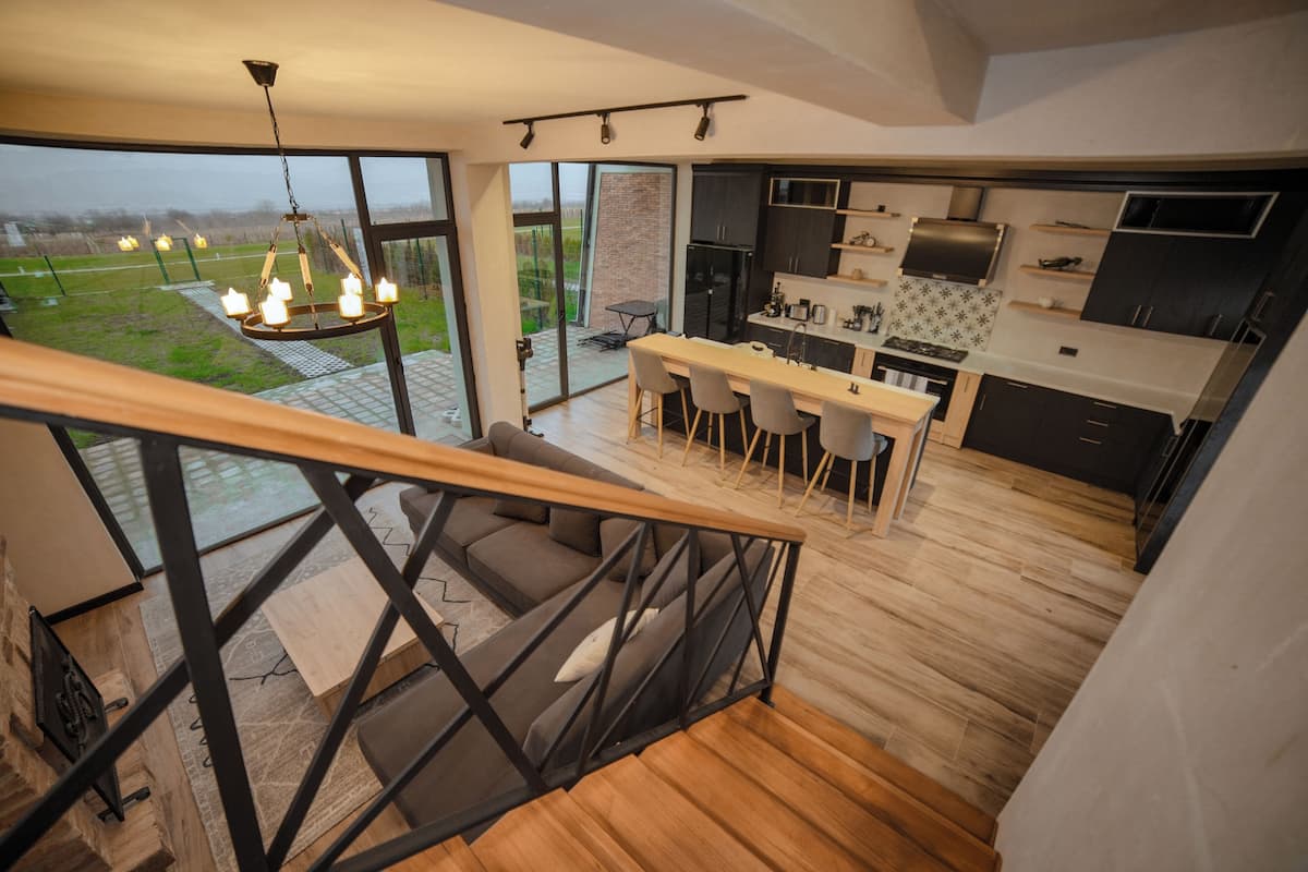 A modern kitchen with dark cabinets, a central island, and a view of a green landscape through large windows.