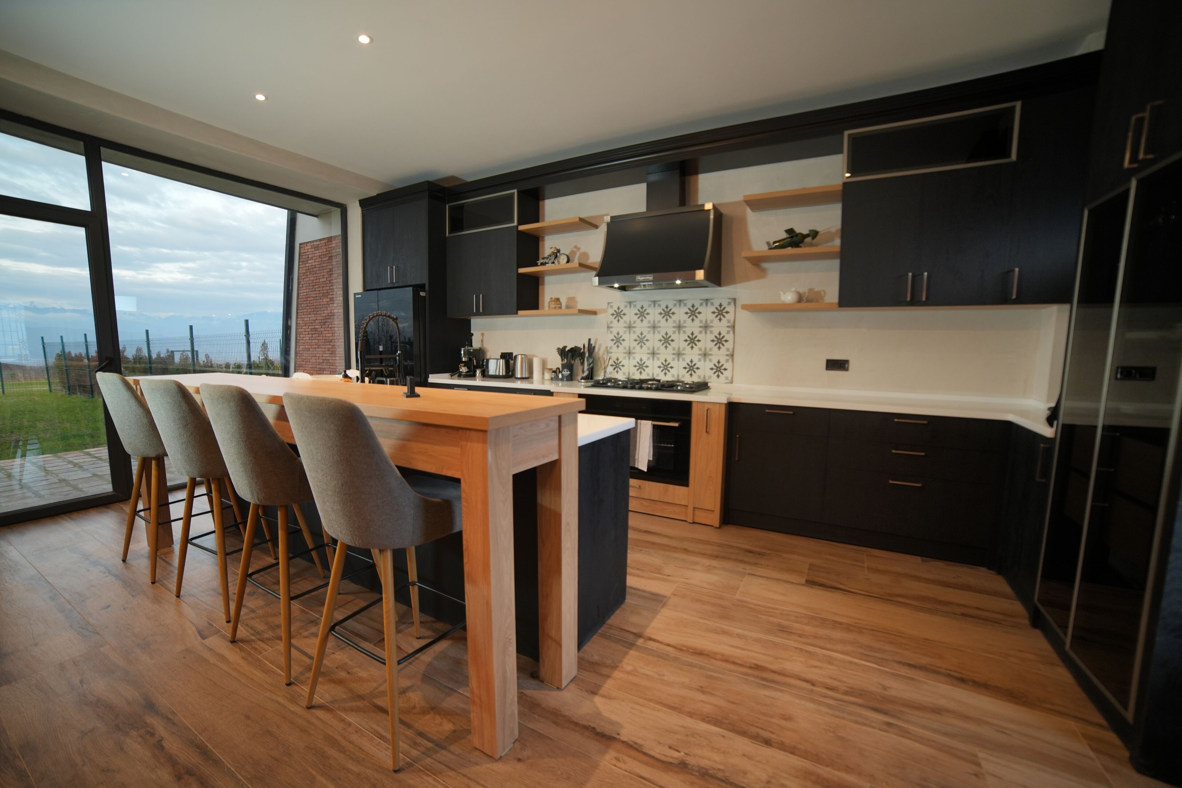 Cocina moderna con una isla grande, armarios oscuros y vistas a través de un ventanal.