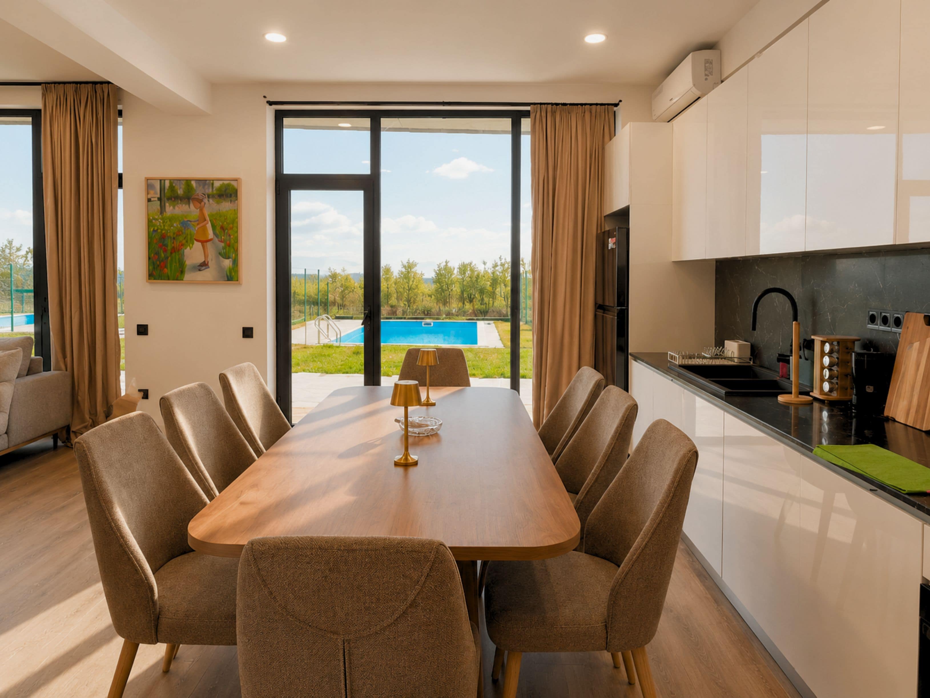 Un comedor moderno con una mesa y sillas, una cocina con pileta y estufa, y vista a una piscina a través de grandes ventanales.