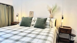 A neatly made bed with a checkered bedspread and two pillows, flanked by bedside tables with lamps. - Quebec City Spa Apt w/Hot Tub & EV Charger (Québec City)