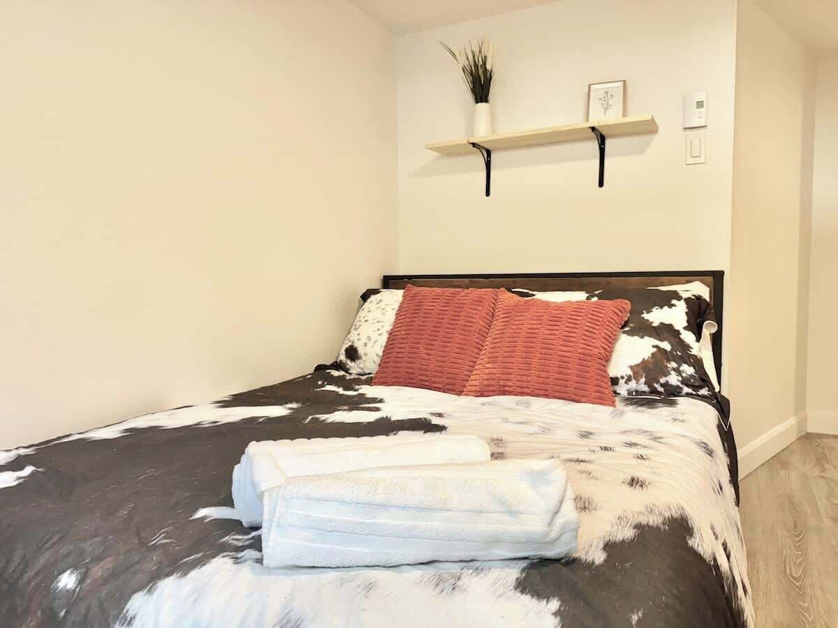 A neatly made bed with a cow print bedspread, a red pillow, and a folded white blanket on a wooden floor.