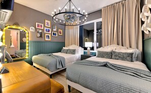 Quarto de hotel com duas camas, um lustre, uma toucador iluminada e um espelho.