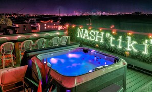 A rooftop terrace with a hot tub, chairs, and a neon sign reading "NASH TIKI".