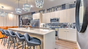 A modern kitchen with a central island, bar stools, stainless steel appliances, and decorative wall tiles. - Lux Nash Escape•11 Beds•Hot Tub•Game Room + Pool+ Pickleball (Nashville)