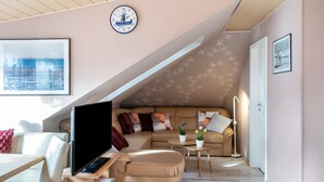 Een woonkamer met een bank, een bijzettafeltje, een televisie en een klok aan de muur.
