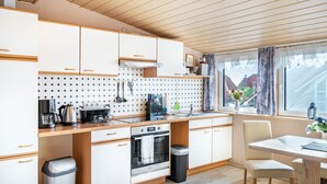 Een moderne keuken met houten kastjes, een inbouwoven en een eethoek met een tafel en stoelen.