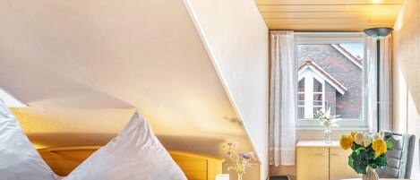 Ein Schlafzimmer mit einem Bett, einem Nachttisch und einem Fenster mit Blick auf ein Backsteingebäude.