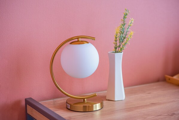 En modern lampa med en sfärisk lampskärm och en guldfärgad fot, placerad på en träyta bredvid en vit vas med gula blommor.
