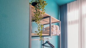 A room with teal walls, a wooden shelf with towels, a hanging plant, and a black hanger. - HB Freeze Inn (Tbilisi)