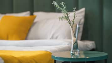 A bed with white and yellow bedding, a glass vase with a plant, and a round table beside the bed.