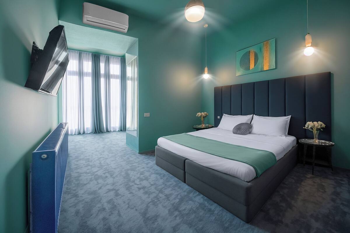 Habitació d'hotel moderna amb un llit gran, un televisor de pantalla plana muntat a la pared i una petita taula auxiliar amb un ram de flors.