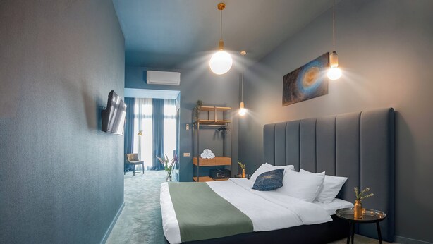 A modern hotel room with a large bed, a bedside table, a wall-mounted TV, and a ceiling light fixture. - HB Freeze Inn (Tbilisi)