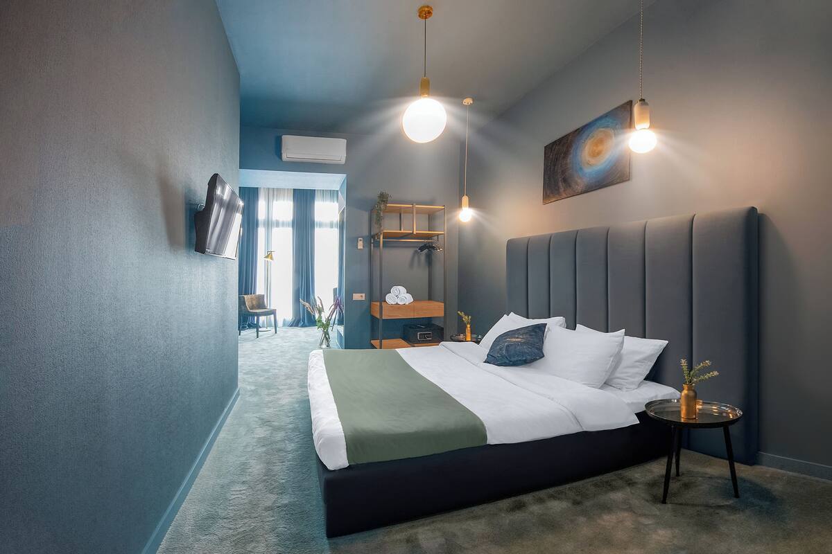 Habitació d'hotel moderna amb un llit gran, una tauleta de nit, un televisor penjat a la paret i una làmpada al sostre.