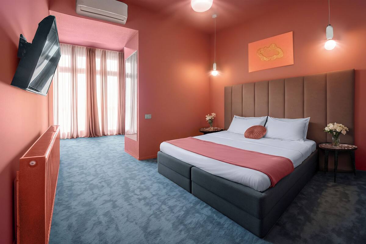 Habitació d'hotel moderna amb un llit gran, un televisor de pantalla plana fixat a la paret, una tauleta de nit amb un ram de flors i una lluminària de sostre.
