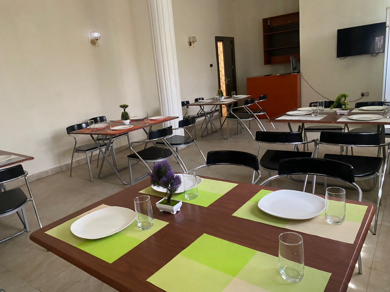 Ein Essbereich mit Tischen für vier Personen, jeder Tisch ist mit einem weißen Teller, einem Glas und einem kleinen Topfpflanzen geschmückt.