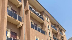 Un hôtel à plusieurs étages, doté d’une façade beige, de balcons et d’un espace d’entrée couvert agrémenté de plantes en pot.