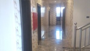 Un couloir au sol de marbre, avec une rambarde en métal et un panneau rouge accroché au mur.